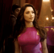 a woman in a purple dress is standing in a room with a man behind her .