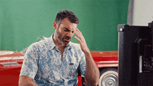 a man in a hawaiian shirt holds his head
