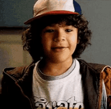 a young boy with curly hair is wearing a baseball cap and a jacket .