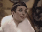 a woman with short hair is wearing a white fur coat .