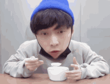a young man wearing a blue hat is eating from a white bowl