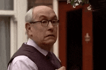 an older man wearing glasses is standing in front of a red door .