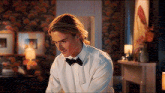 a man in a white shirt and black bow tie is sitting in a living room