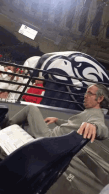 a man sits in a stadium watching a game with a mascot behind him that says ucsd on it
