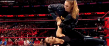 two women are wrestling in a ring with a crowd watching .