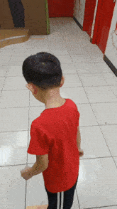 a young boy in a red shirt is standing on a tiled floor