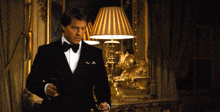 a man in a tuxedo is standing in a room with a lamp