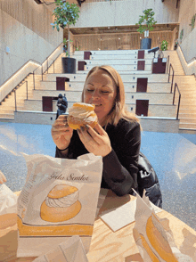 a woman sitting at a table eating a pastry from a bag that says " guda sandels "