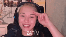 a woman wearing headphones is smiling with the word zatim written on her forehead
