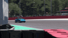 a blue car is driving down a race track with a red fence behind it