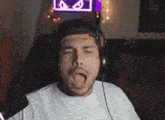 a man wearing headphones is covering his eyes with his hands while sitting in front of a neon sign with eyes .