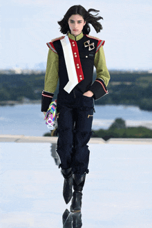 a model walks down the runway at a fashion show wearing a jacket with a cross on it