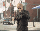 a woman in a black jacket is covering her face with her hands