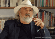 a man with a beard wearing a hat and smoking a cigar with the name milenko makedonski below him