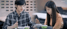 a man and a woman are sitting at a table eating bowls of soup .