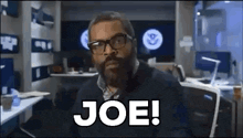 a man with a beard and glasses is sitting in front of a computer and says joe !