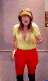 a woman wearing a yellow shirt and red shorts is standing in front of a wall