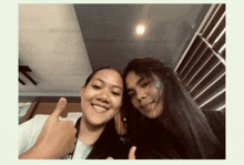 two young women are posing for a picture together and one of them is giving a thumbs up .