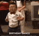 a little boy is dancing at a birthday party while wearing suspenders and a bow tie .