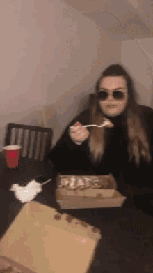 a woman wearing sunglasses is sitting at a table eating a slice of pizza
