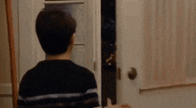 a boy is standing in a doorway looking at another boy holding a bottle of beer .