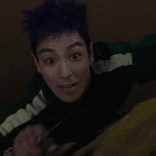 a man with purple hair is smiling while holding a cross with the word jesus on it
