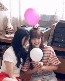 two girls sitting next to each other with a pink balloon on top of one of them