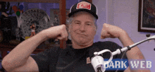 a man is flexing his muscles in front of a microphone while wearing a hat and a shirt that says dark web