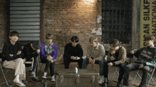 a group of young men are sitting in front of a brick wall with a sign that says ' korean silk ' on it