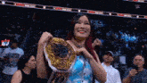 a woman is holding a wrestling championship belt in front of a crowd of people