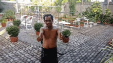 a man without a shirt is giving a thumbs up in front of potted plants