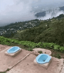 two blue toilets are sitting on top of a concrete platform overlooking a valley