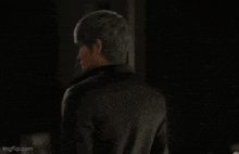 a man in a black jacket is standing in the dark looking at the camera .