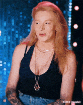 a woman wearing a black tank top and a gold necklace has a tattoo on her arm ..