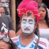 a man with a red hat and white face paint is standing in a crowd .