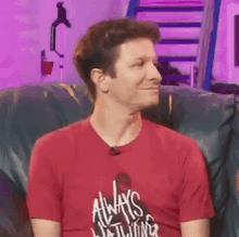 a man is sitting on a couch wearing a red shirt that says `` always watching '' .