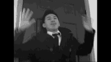 a man in a suit and tie is standing in front of a door with his hands up .
