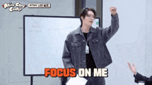 a man in a denim jacket stands in front of a white board and says " focus on me "