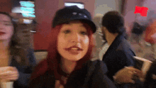 a woman with red hair is wearing a black hat and making a funny face