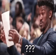 a man in a suit is holding a piece of paper in front of a crowd and asking a question .