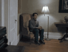 a man is sitting in a chair in a room with a lamp