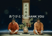 two people are kneeling in front of a sign that says " thank you "