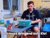 a man sits at a table with a box on it that says ich muss dringend aufs klo on it