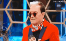 a man wearing sunglasses and a red jacket is sitting in front of a screen that says thesfigato .