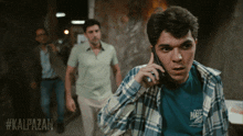 a man in a plaid shirt is talking on a cell phone while another man looks on
