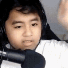 a young boy wearing headphones and a white shirt is standing in front of a microphone .