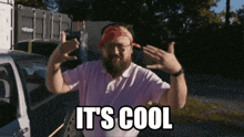 a man with a bandana on his head is standing in front of a car with the words " it 's cool " on the bottom