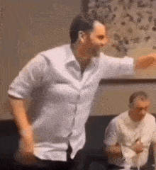 a man in a white shirt is dancing in a room while another man looks on .