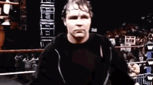 a man in a black shirt is standing in a wrestling ring with a crowd watching .