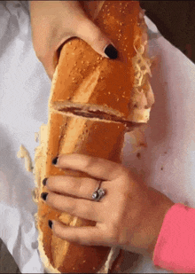 a woman with a ring on her finger holds a long sandwich